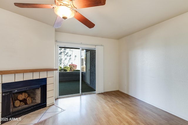 living area with light wood-type flooring, ceiling fan, a tiled fireplace, and baseboards