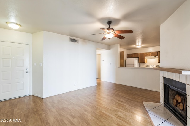 unfurnished living room with ceiling fan, a tile fireplace, and light wood-type flooring