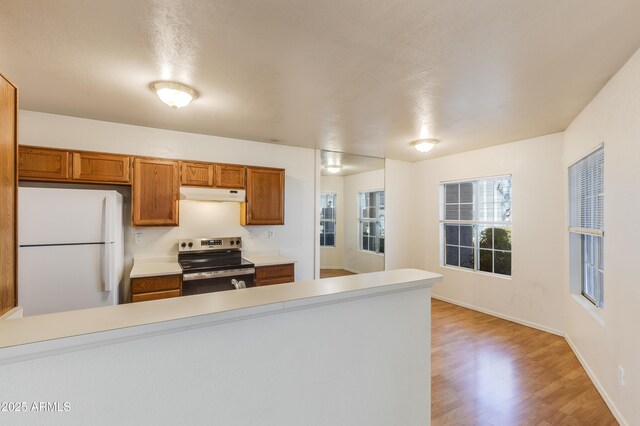 kitchen featuring light countertops, under cabinet range hood, stainless steel electric range oven, and freestanding refrigerator