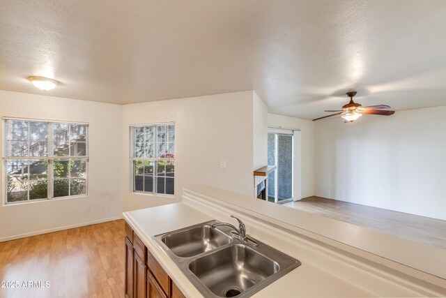 kitchen featuring ceiling fan, brown cabinetry, a sink, light countertops, and light wood finished floors