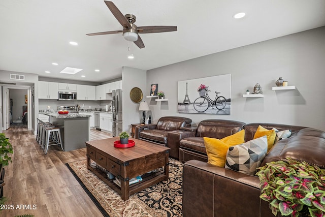 living room featuring visible vents, light wood-style flooring, recessed lighting, a skylight, and ceiling fan