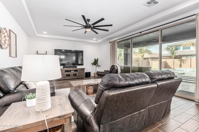 living room with ceiling fan, visible vents, a raised ceiling, and recessed lighting