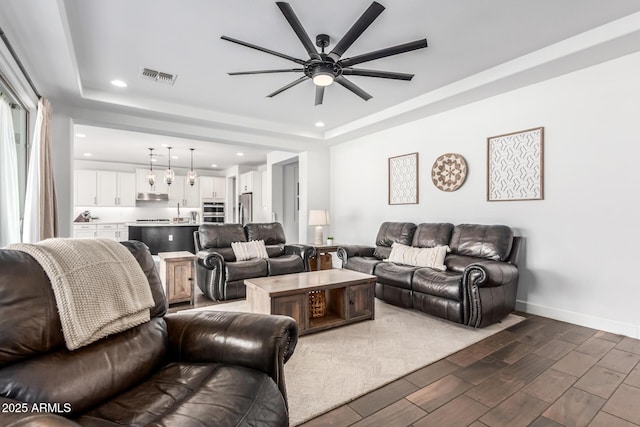 living area with a tray ceiling, visible vents, baseboards, and wood finish floors