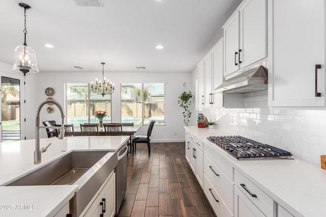 kitchen with white cabinets, decorative backsplash, appliances with stainless steel finishes, under cabinet range hood, and a notable chandelier