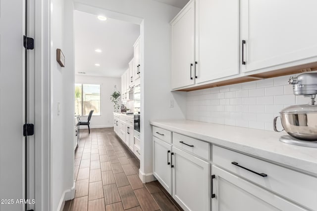 kitchen featuring tasteful backsplash, recessed lighting, wood tiled floor, white cabinetry, and light stone countertops