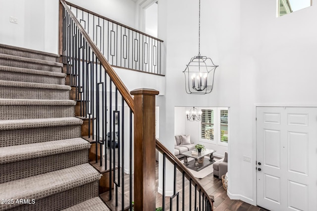 staircase featuring wood finished floors, a towering ceiling, baseboards, and an inviting chandelier