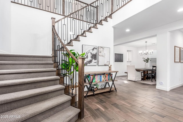 stairway with a notable chandelier, recessed lighting, a high ceiling, wood finished floors, and baseboards