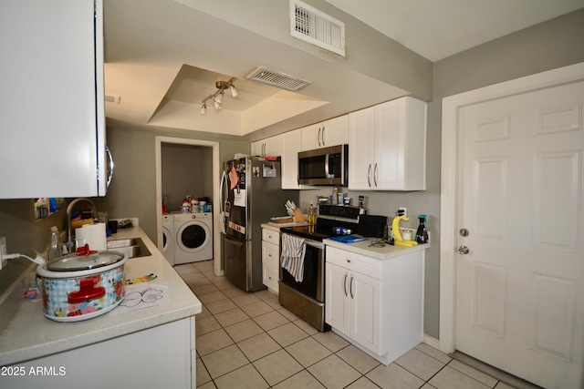 kitchen featuring visible vents, washer and clothes dryer, a tray ceiling, appliances with stainless steel finishes, and a sink