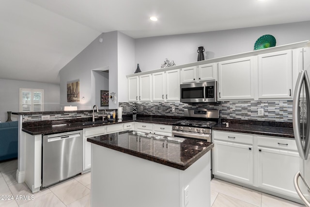 kitchen with sink, a center island, dark stone counters, vaulted ceiling, and appliances with stainless steel finishes