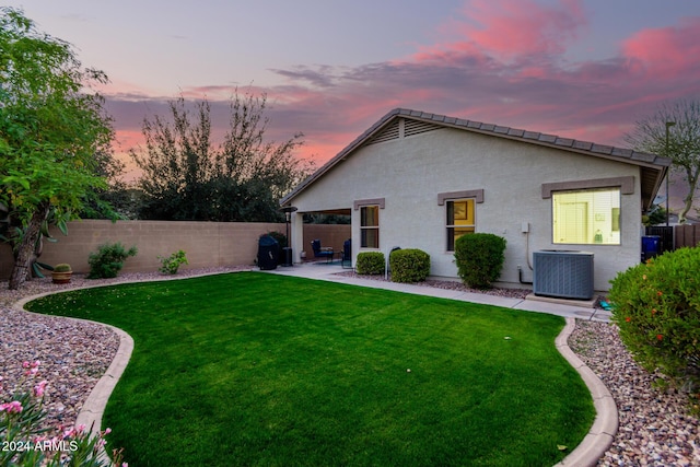 back house at dusk featuring central AC unit, a patio area, and a lawn