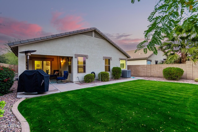 back house at dusk with a lawn, a patio area, and central air condition unit