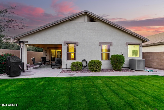 back house at dusk with a lawn, a patio area, and central AC unit