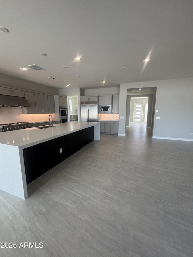 kitchen featuring under cabinet range hood, backsplash, a spacious island, light countertops, and built in appliances