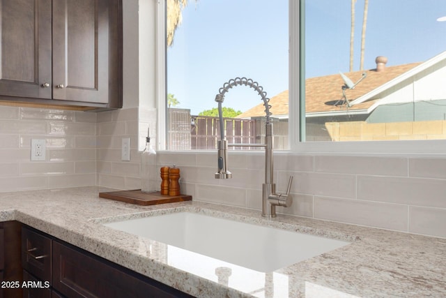 interior details with dark brown cabinetry, light stone countertops, sink, and backsplash