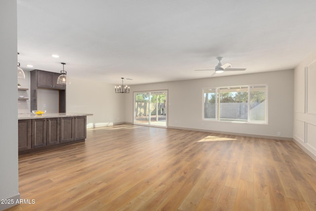 unfurnished living room featuring ceiling fan with notable chandelier and light hardwood / wood-style floors