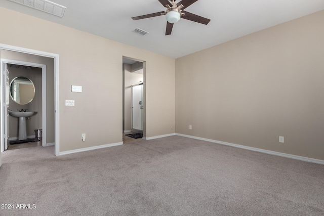 unfurnished bedroom featuring sink, ceiling fan, light carpet, and ensuite bath