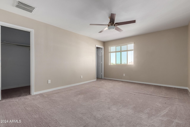 unfurnished bedroom featuring light carpet, a walk in closet, and ceiling fan