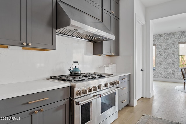 kitchen featuring gray cabinets, double oven range, light hardwood / wood-style flooring, and wall chimney exhaust hood