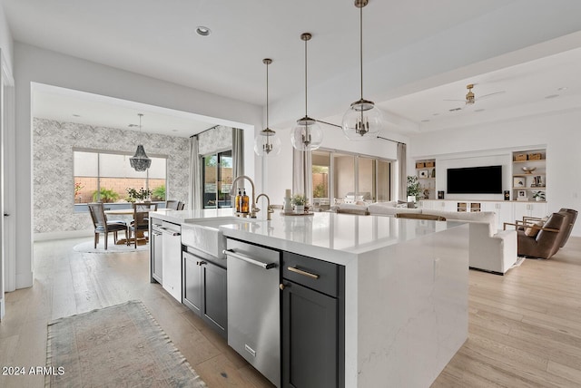 kitchen featuring sink, hanging light fixtures, a kitchen island with sink, stainless steel dishwasher, and light wood-type flooring