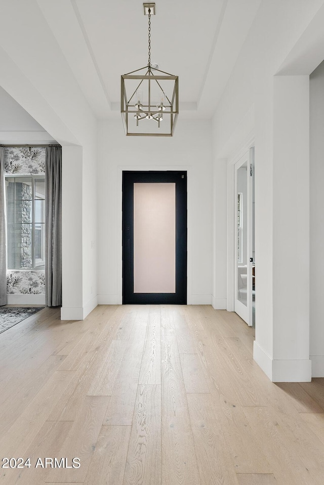 entryway with a raised ceiling, hardwood / wood-style floors, and a notable chandelier