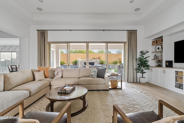 living room featuring a tray ceiling, built in shelves, wine cooler, and light wood-type flooring