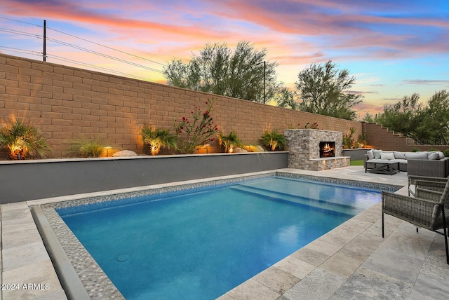 pool at dusk featuring an outdoor living space with a fireplace and a patio