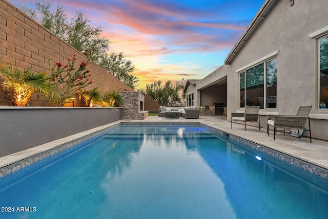 pool at dusk featuring area for grilling, an outdoor living space with a fireplace, and a patio area