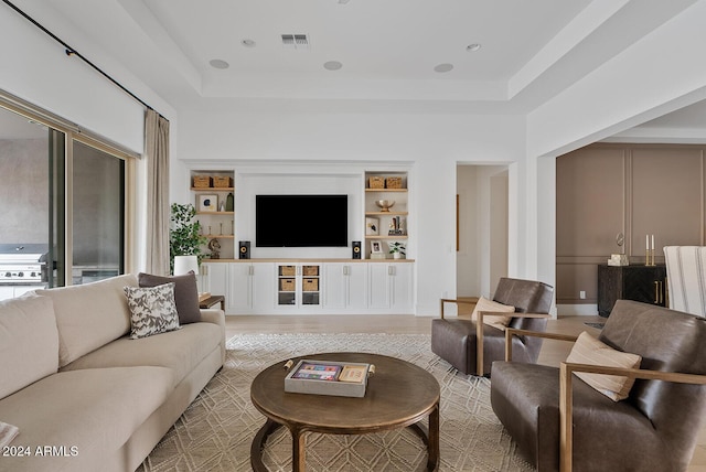 living room featuring a tray ceiling, a towering ceiling, light hardwood / wood-style floors, and built in shelves