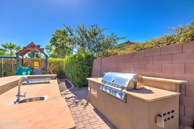 view of patio featuring a playground, grilling area, sink, and exterior kitchen