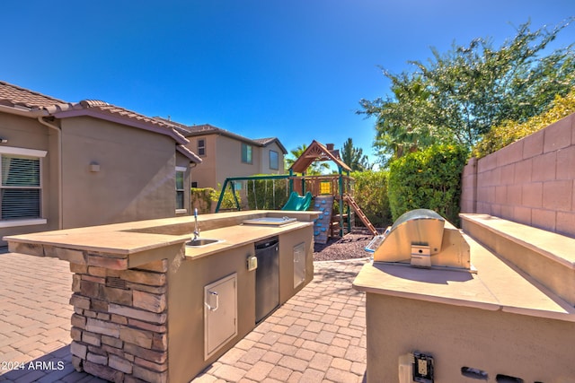 view of patio featuring a playground, sink, and an outdoor kitchen