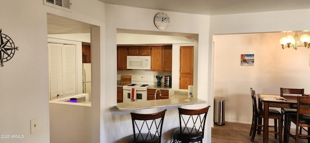 kitchen featuring kitchen peninsula, white appliances, dark wood-type flooring, a notable chandelier, and hanging light fixtures