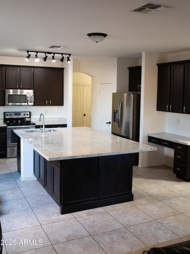 kitchen with sink, appliances with stainless steel finishes, light stone countertops, an island with sink, and light tile patterned flooring