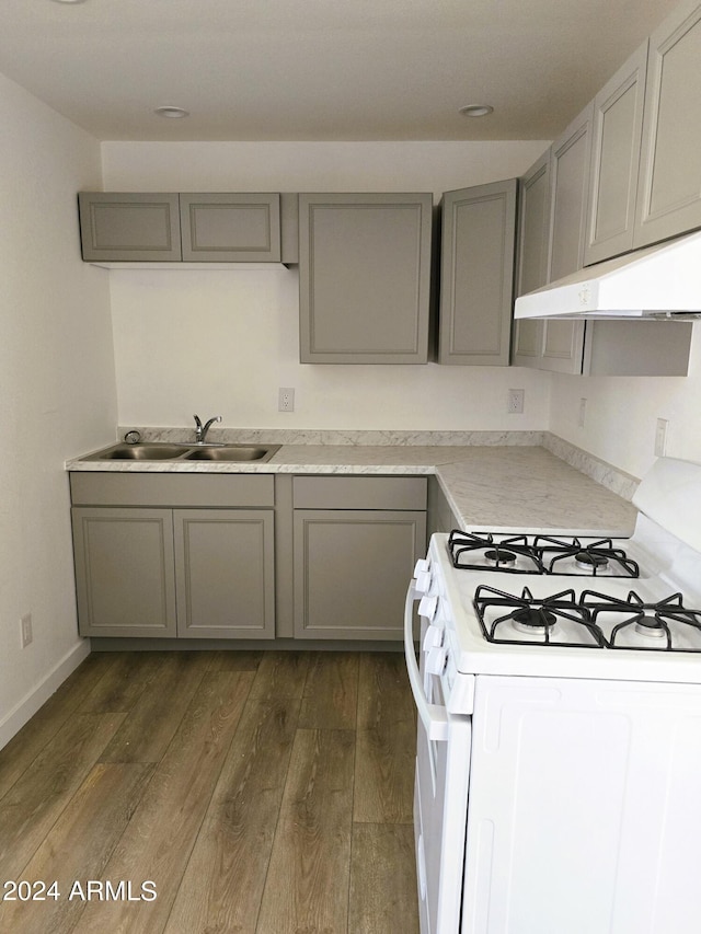 kitchen featuring gray cabinetry, under cabinet range hood, a sink, dark wood finished floors, and white gas range oven