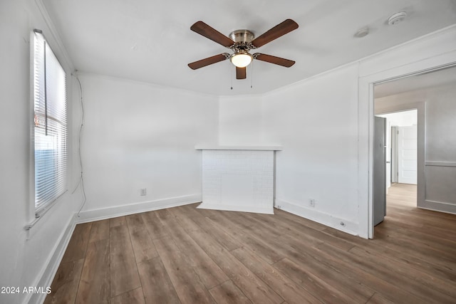 empty room with baseboards, a brick fireplace, wood finished floors, and crown molding