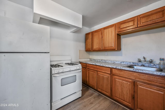 kitchen featuring white appliances, wood finished floors, brown cabinets, and a sink