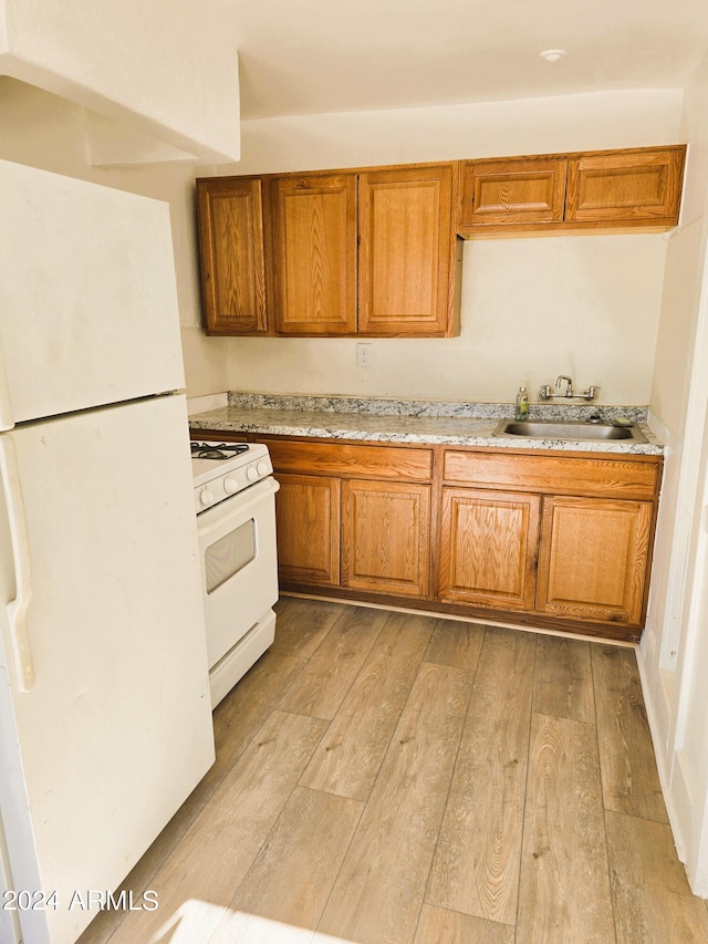 kitchen with brown cabinets, white appliances, light wood-style floors, and a sink