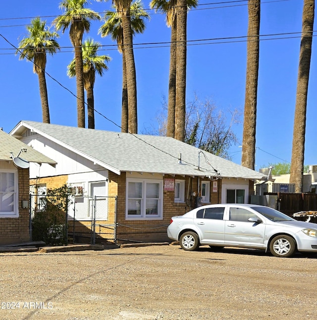 view of front of home with fence, brick siding, a shingled roof, and a gate