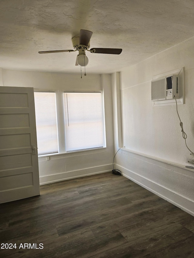 unfurnished room with baseboards, a textured ceiling, an AC wall unit, and dark wood-style flooring