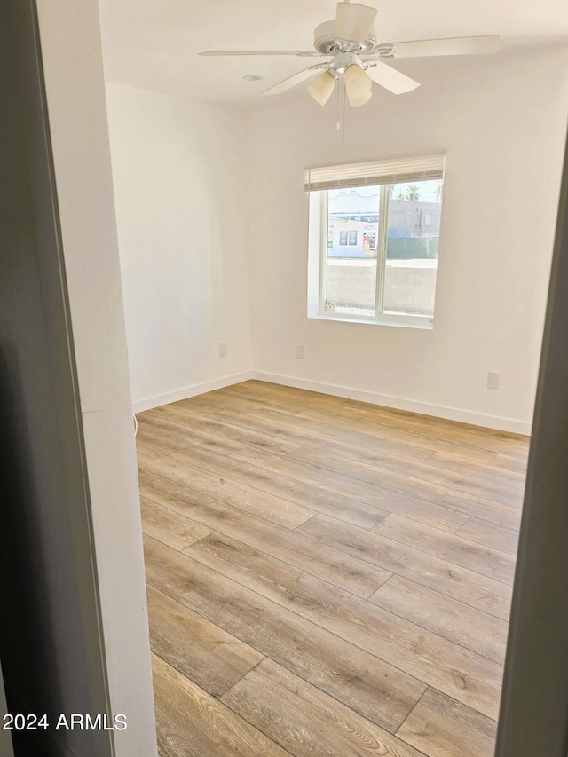 spare room with baseboards, light wood-style floors, and ceiling fan