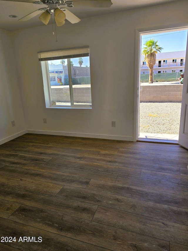 empty room featuring a wealth of natural light, baseboards, and dark wood-style flooring