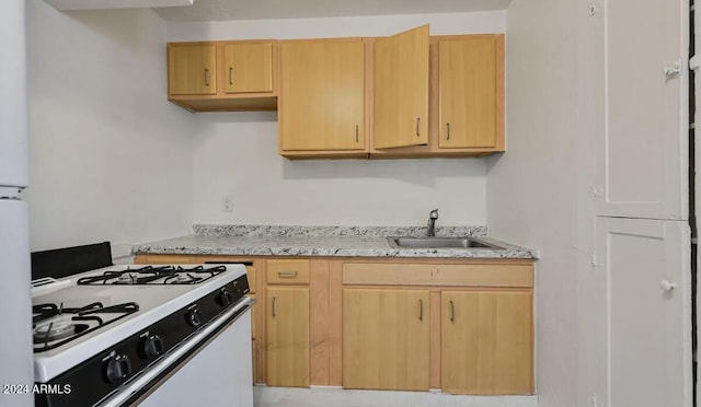 kitchen featuring white range with gas cooktop, light brown cabinets, light stone countertops, and a sink