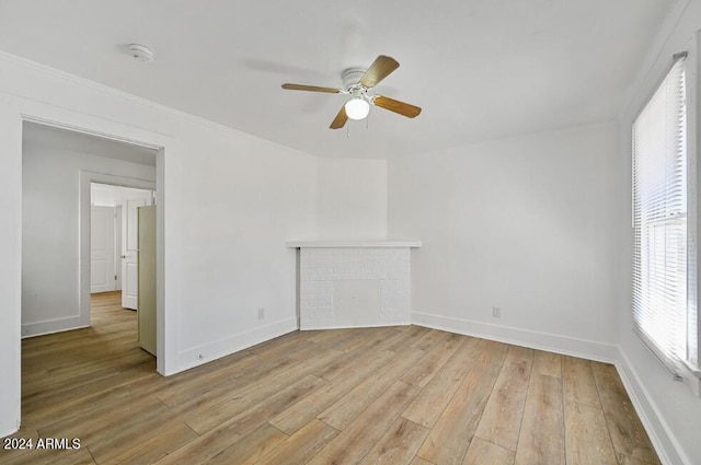 unfurnished room featuring a ceiling fan, a fireplace, baseboards, and light wood finished floors