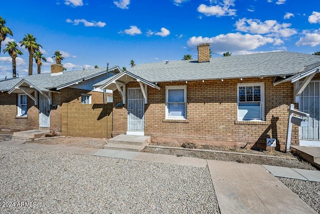 view of front of home with brick siding, a chimney, roof with shingles, and fence