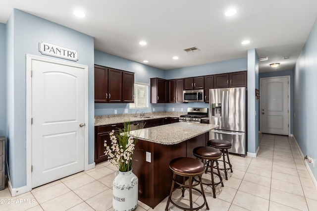 kitchen with stainless steel appliances, sink, a center island, a breakfast bar area, and light stone countertops