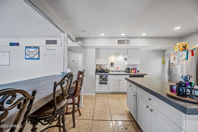 kitchen with backsplash, white cabinets, sink, light tile patterned floors, and stainless steel refrigerator