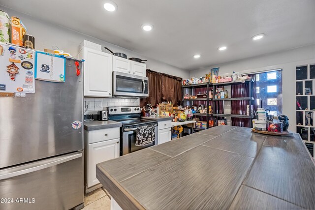 kitchen with light tile patterned floors, stainless steel appliances, white cabinetry, and tasteful backsplash