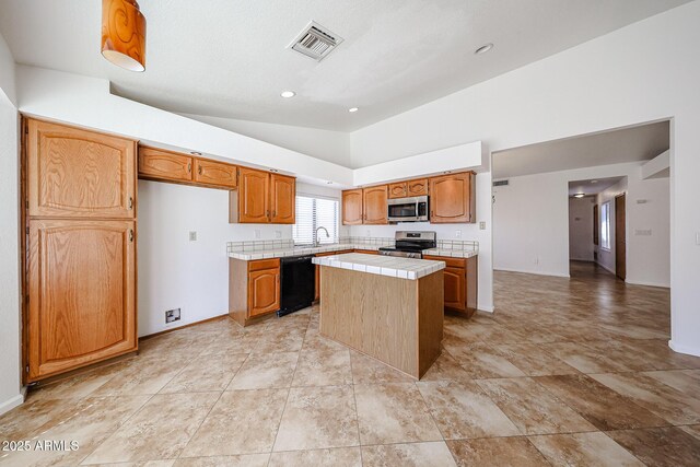 kitchen featuring visible vents, a center island, tile counters, vaulted ceiling, and stainless steel appliances