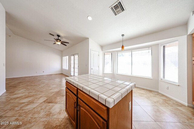 kitchen featuring visible vents, a kitchen island, tile countertops, vaulted ceiling, and a ceiling fan