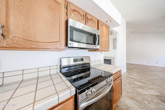 kitchen with light tile patterned floors, baseboards, appliances with stainless steel finishes, and tile counters