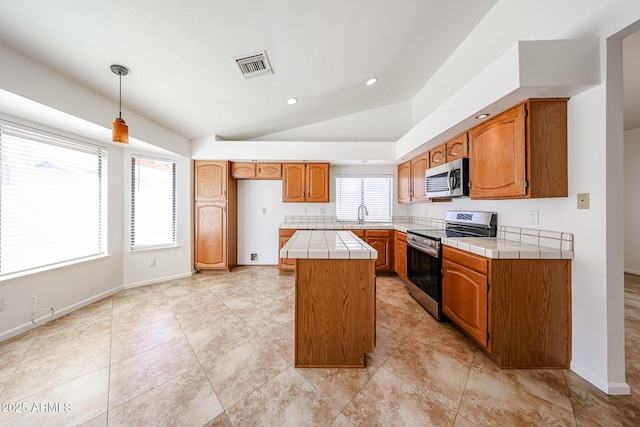 kitchen featuring visible vents, a kitchen island, tile counters, lofted ceiling, and stainless steel appliances